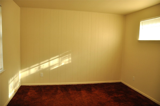 unfurnished room featuring dark colored carpet and wooden walls