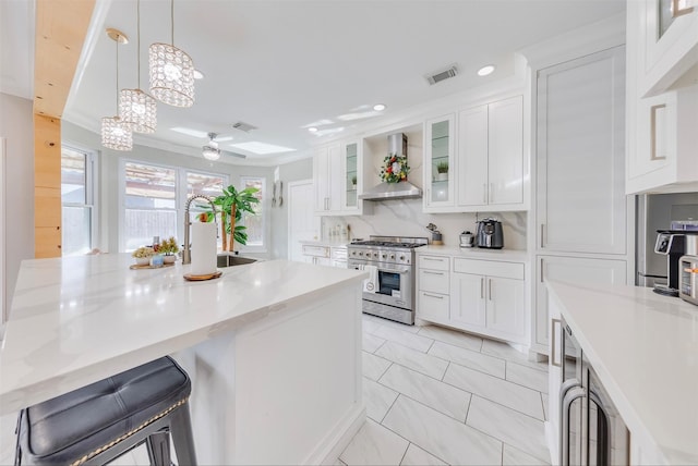 kitchen featuring pendant lighting, white cabinets, sink, high end stainless steel range, and wall chimney exhaust hood