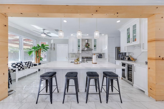 kitchen with white cabinetry, wall chimney range hood, wine cooler, a spacious island, and decorative light fixtures