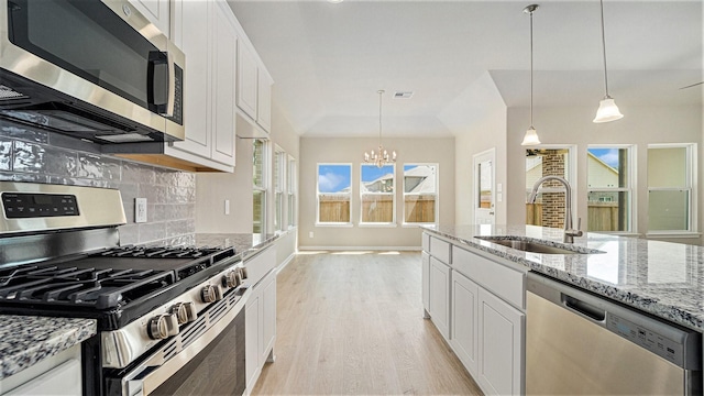 kitchen with appliances with stainless steel finishes, sink, a notable chandelier, white cabinetry, and hanging light fixtures