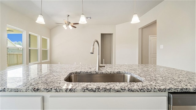 kitchen with vaulted ceiling, decorative light fixtures, light stone counters, and sink