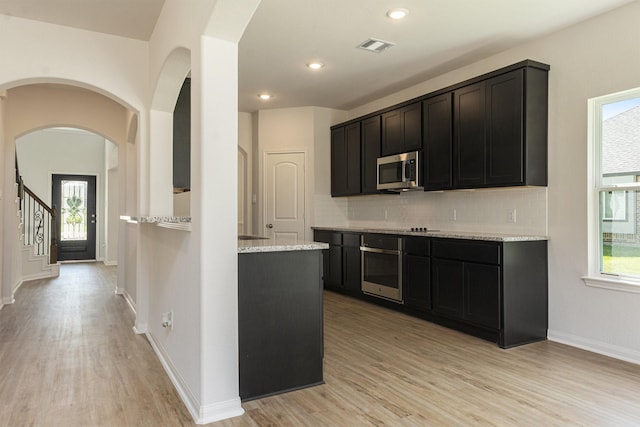 kitchen featuring light wood-type flooring, stainless steel appliances, tasteful backsplash, and a healthy amount of sunlight