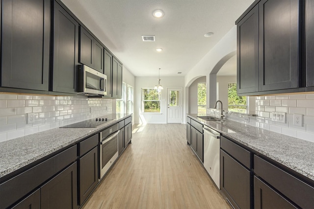 kitchen with light stone countertops, sink, light hardwood / wood-style floors, decorative backsplash, and appliances with stainless steel finishes