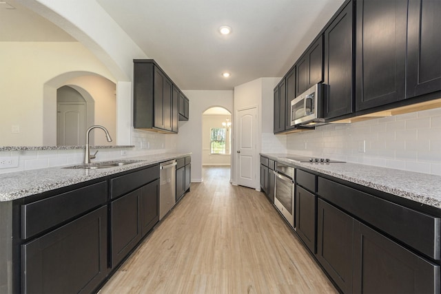 kitchen featuring appliances with stainless steel finishes, backsplash, light stone counters, sink, and light hardwood / wood-style flooring