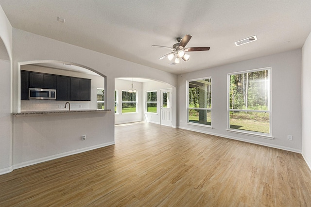 unfurnished living room with hardwood / wood-style floors, ceiling fan with notable chandelier, sink, and a textured ceiling