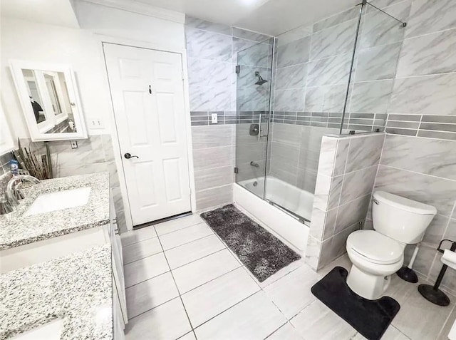 full bathroom with shower / bath combination with glass door, tile patterned floors, vanity, and tile walls