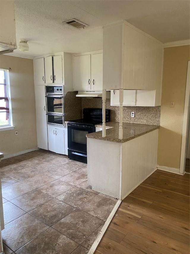 kitchen with stainless steel oven, hardwood / wood-style flooring, dark stone countertops, black / electric stove, and white cabinetry