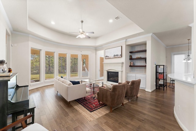 living room featuring a tray ceiling, ceiling fan with notable chandelier, dark hardwood / wood-style floors, and ornamental molding