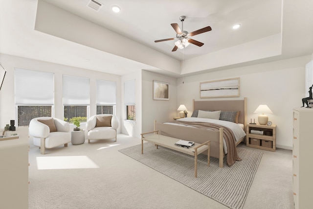 bedroom with ceiling fan, light carpet, and a tray ceiling