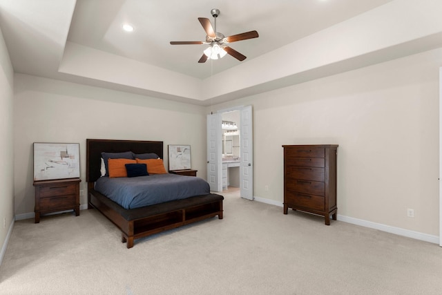 bedroom featuring a raised ceiling, ensuite bath, ceiling fan, and light colored carpet