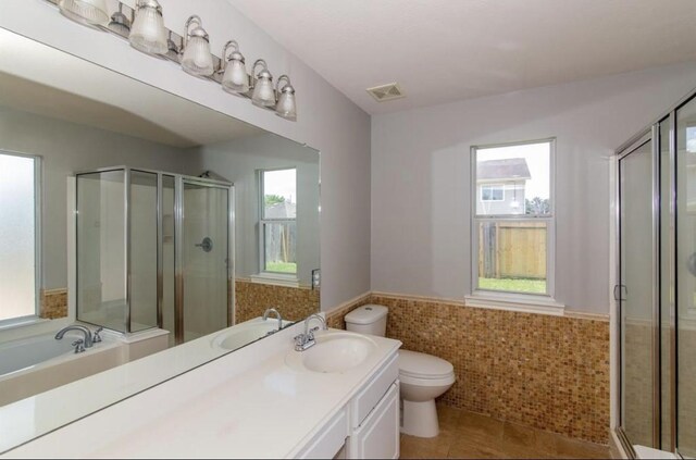 bathroom featuring tile patterned flooring, toilet, a shower with door, vanity, and tile walls