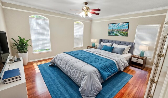 bedroom with hardwood / wood-style flooring, ceiling fan, ornamental molding, and multiple windows