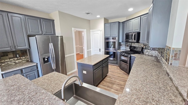 kitchen with decorative backsplash, appliances with stainless steel finishes, sink, a center island, and light hardwood / wood-style floors