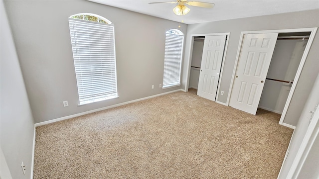 unfurnished bedroom featuring carpet, ceiling fan, and multiple closets