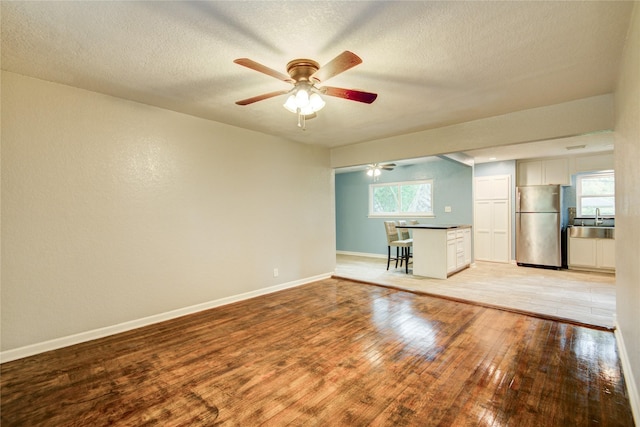 unfurnished living room featuring a textured ceiling, light wood-type flooring, ceiling fan, and sink