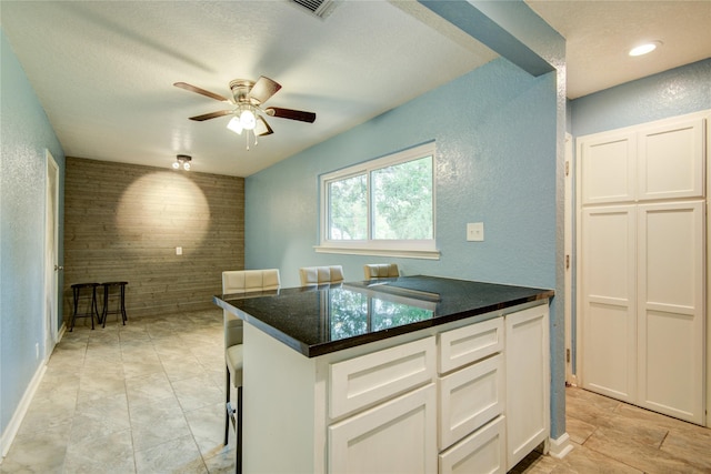 kitchen featuring white cabinetry, ceiling fan, a kitchen breakfast bar, a textured ceiling, and light tile patterned flooring