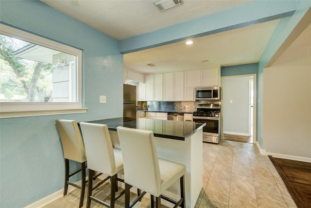 kitchen with a kitchen breakfast bar, tasteful backsplash, white cabinetry, kitchen peninsula, and stainless steel appliances