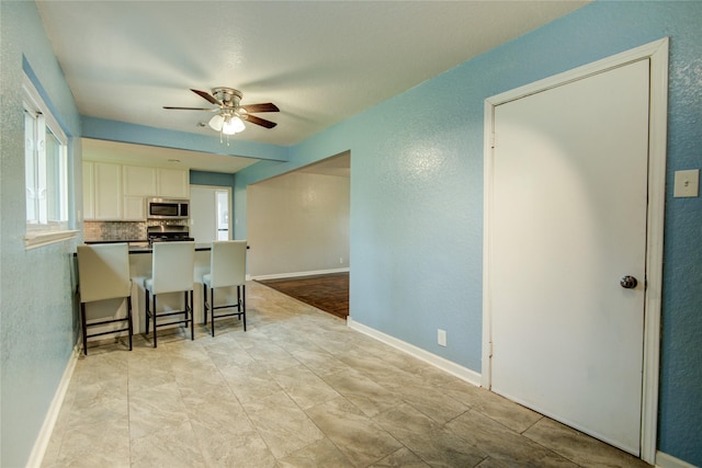 kitchen featuring ceiling fan, decorative backsplash, appliances with stainless steel finishes, white cabinetry, and a breakfast bar area