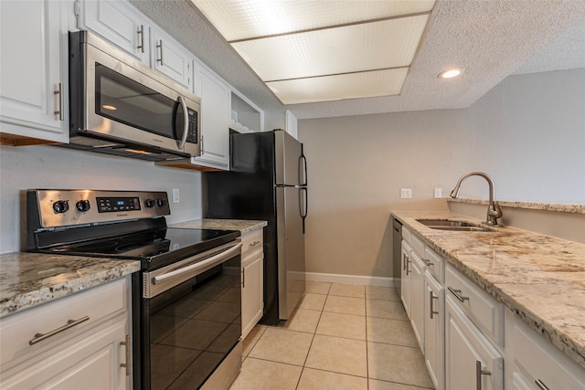 kitchen with sink, stainless steel appliances, light tile patterned floors, a textured ceiling, and white cabinets