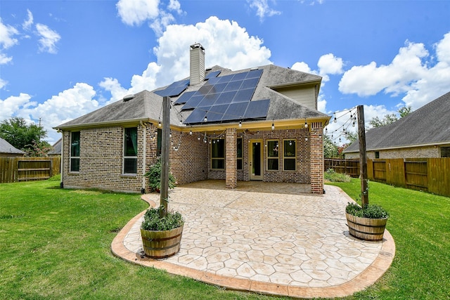 back of property with solar panels, a patio, and a lawn