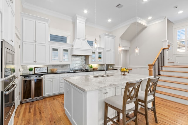 kitchen with stainless steel appliances, sink, decorative light fixtures, a center island with sink, and white cabinetry