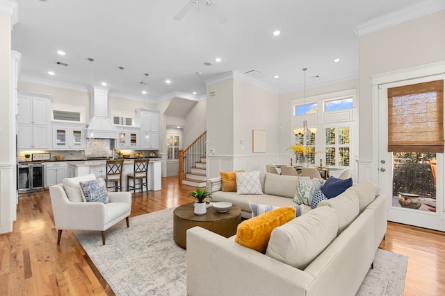 living room with ceiling fan with notable chandelier, light hardwood / wood-style floors, wine cooler, and ornamental molding