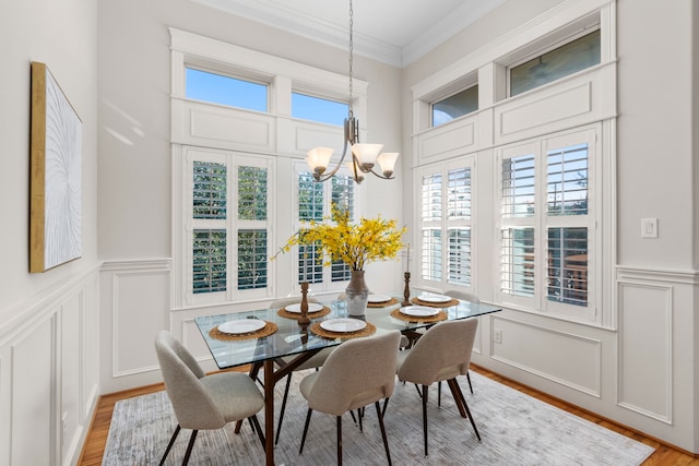 dining area with light wood-type flooring, ornamental molding, and a notable chandelier