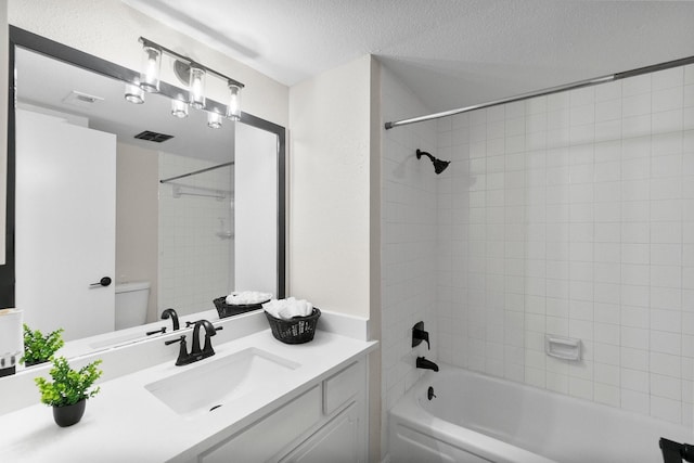 full bathroom featuring vanity, a textured ceiling, tiled shower / bath combo, and toilet