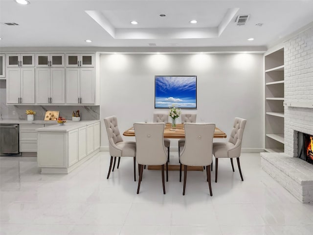 dining room with built in shelves, a raised ceiling, and a fireplace