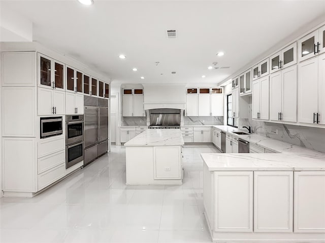 kitchen featuring premium range hood, light stone counters, stainless steel appliances, white cabinetry, and a kitchen island