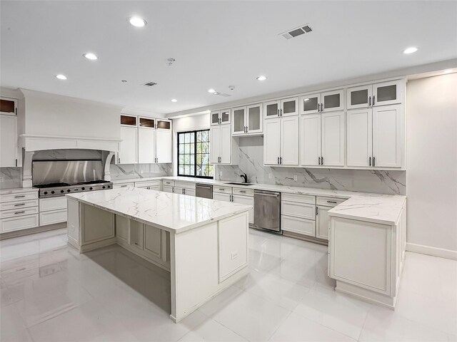 kitchen with decorative backsplash, light stone countertops, white cabinets, dishwasher, and a center island