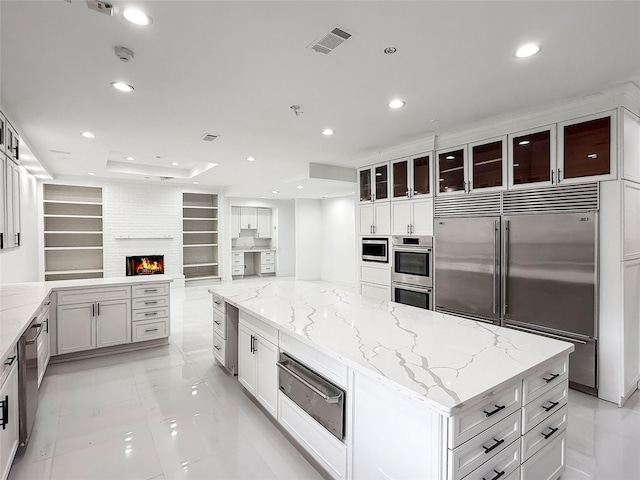 kitchen with light stone countertops, a center island, built in features, built in appliances, and a fireplace