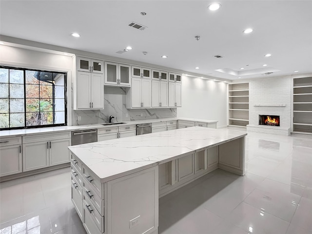 kitchen featuring stainless steel dishwasher, light stone counters, light tile patterned floors, a fireplace, and white cabinetry