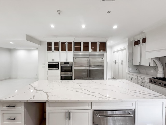 kitchen with built in appliances, light stone countertops, white cabinets, and decorative backsplash