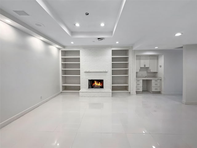 unfurnished living room featuring built in shelves, built in desk, a fireplace, and a tray ceiling