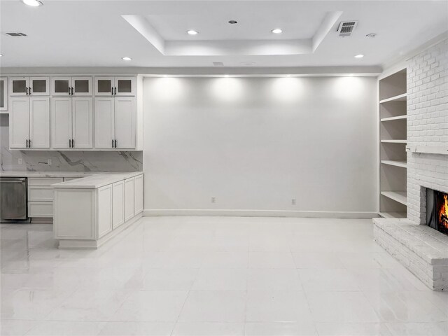 interior space with a tray ceiling, built in features, white cabinets, and a brick fireplace