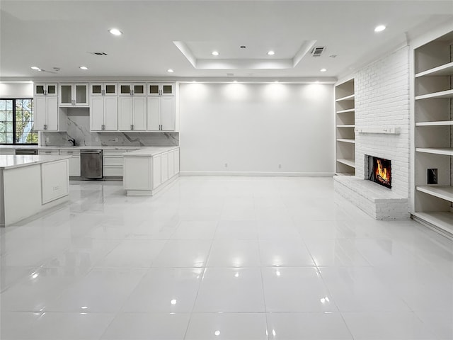 unfurnished living room featuring a raised ceiling, a fireplace, built in features, and sink