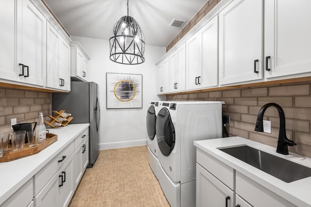 washroom with an inviting chandelier, cabinets, sink, and washing machine and clothes dryer