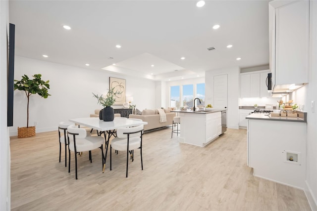 dining area with a raised ceiling, light hardwood / wood-style flooring, and sink