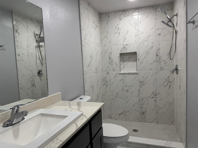 bathroom with a tile shower, vanity, and toilet