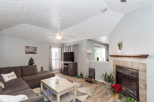 living room with a textured ceiling, a fireplace, light hardwood / wood-style floors, and vaulted ceiling