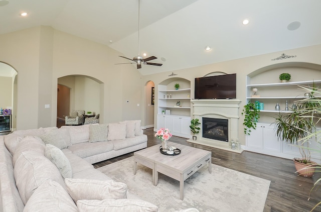 living room with built in shelves, ceiling fan, high vaulted ceiling, and dark wood-type flooring