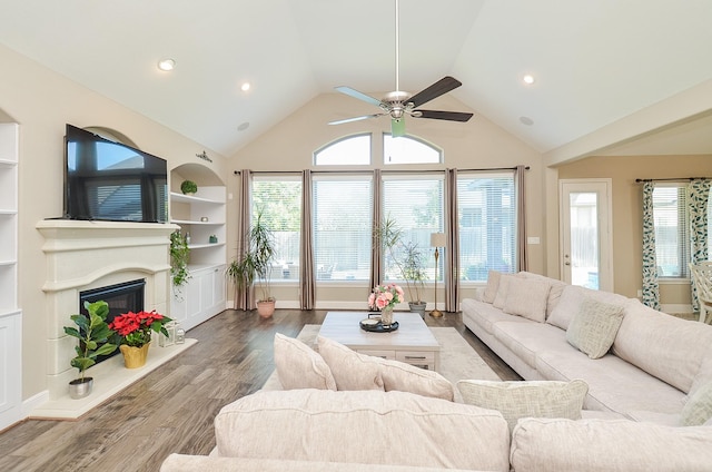 living room with ceiling fan, wood-type flooring, high vaulted ceiling, and built in shelves