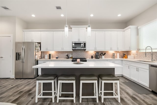 kitchen with a center island, sink, decorative light fixtures, white cabinetry, and stainless steel appliances