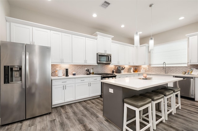 kitchen featuring white cabinets, sink, appliances with stainless steel finishes, decorative light fixtures, and a kitchen island