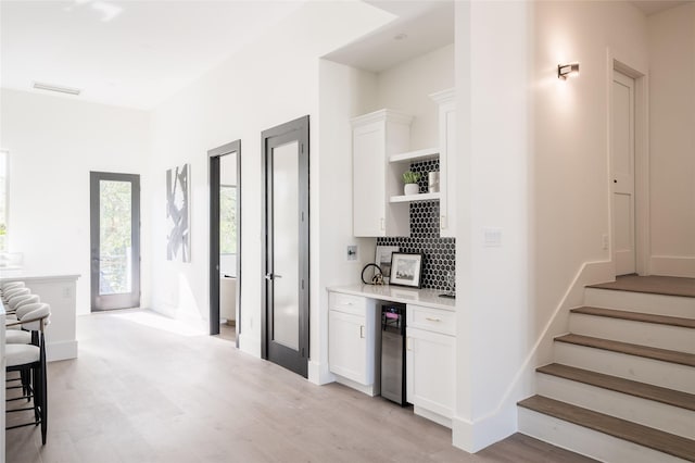 kitchen featuring white cabinets, light hardwood / wood-style flooring, beverage cooler, and tasteful backsplash