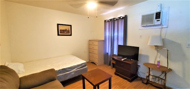 bedroom with light wood-type flooring, a wall unit AC, and ceiling fan