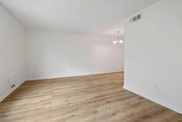 spare room featuring a notable chandelier and light wood-type flooring