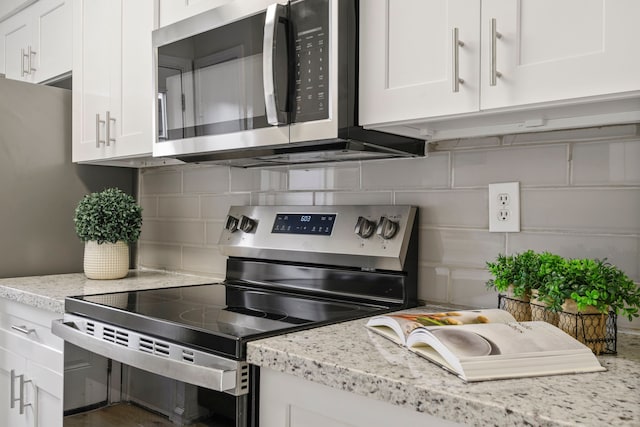 kitchen with backsplash, white cabinetry, stainless steel appliances, and light stone counters