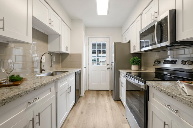 kitchen with white cabinets, sink, light hardwood / wood-style flooring, decorative backsplash, and stainless steel appliances